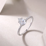 CARISSIE pear moissanite solitaire ring angled shot on textured surface, catching light on silver metal