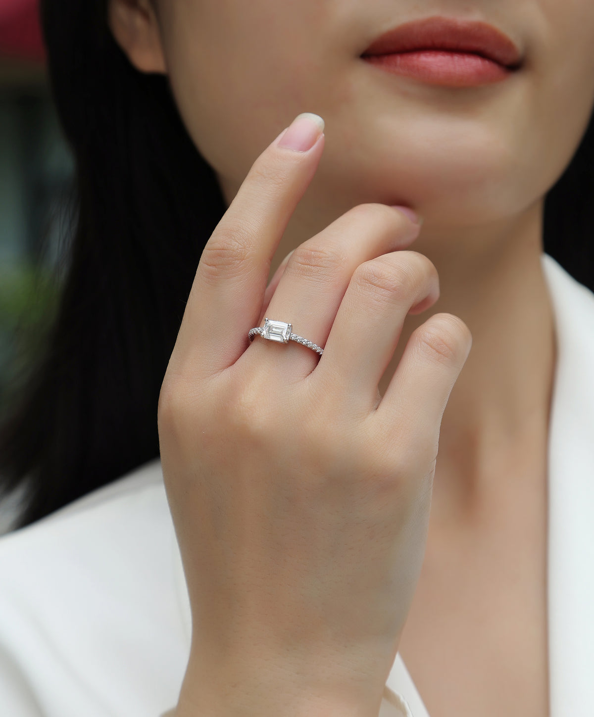 CARISSIE emerald cut solitaire engagement ring on model hand, showing elegant fit and pavé shoulder details