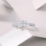 CARISSIE emerald cut solitaire engagement ring styled on textured surface emphasizing geometric lines and sparkle