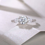 CARISSIE round moissanite solitaire ring, lifestyle shot on textured white surface capturing light reflection in the stones