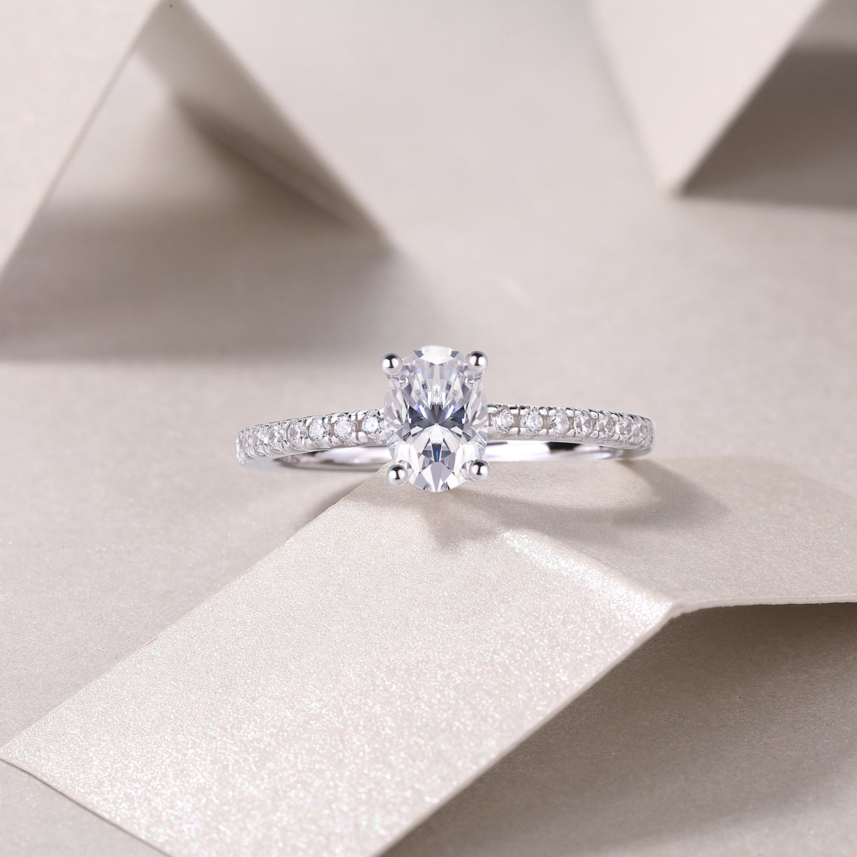 CARISSIE oval moissanite solitaire ring lifestyle shot on textured paper surface, capturing fire and brilliance in soft lighting