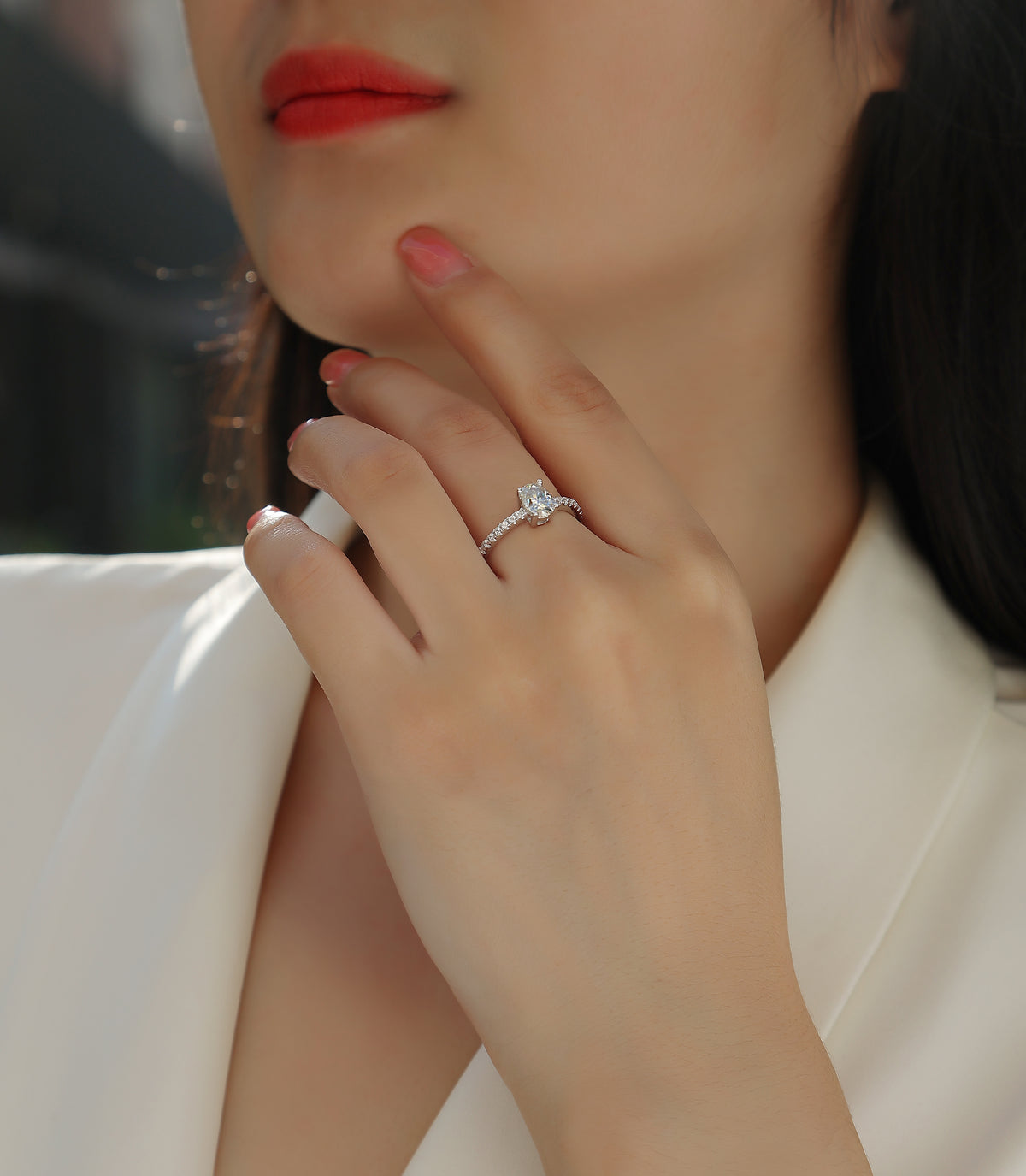 CARISSIE oval moissanite solitaire ring worn by model, touching face to showcase the elegant pavé band and sparkle