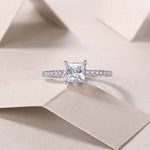 CARISSIE solitaire engagement ring top-down view on paper background, featuring brilliant square stone and delicate band