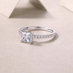 CARISSIE princess cut ring lifestyle shot on textured surface, capturing light reflection on silver metal and facets