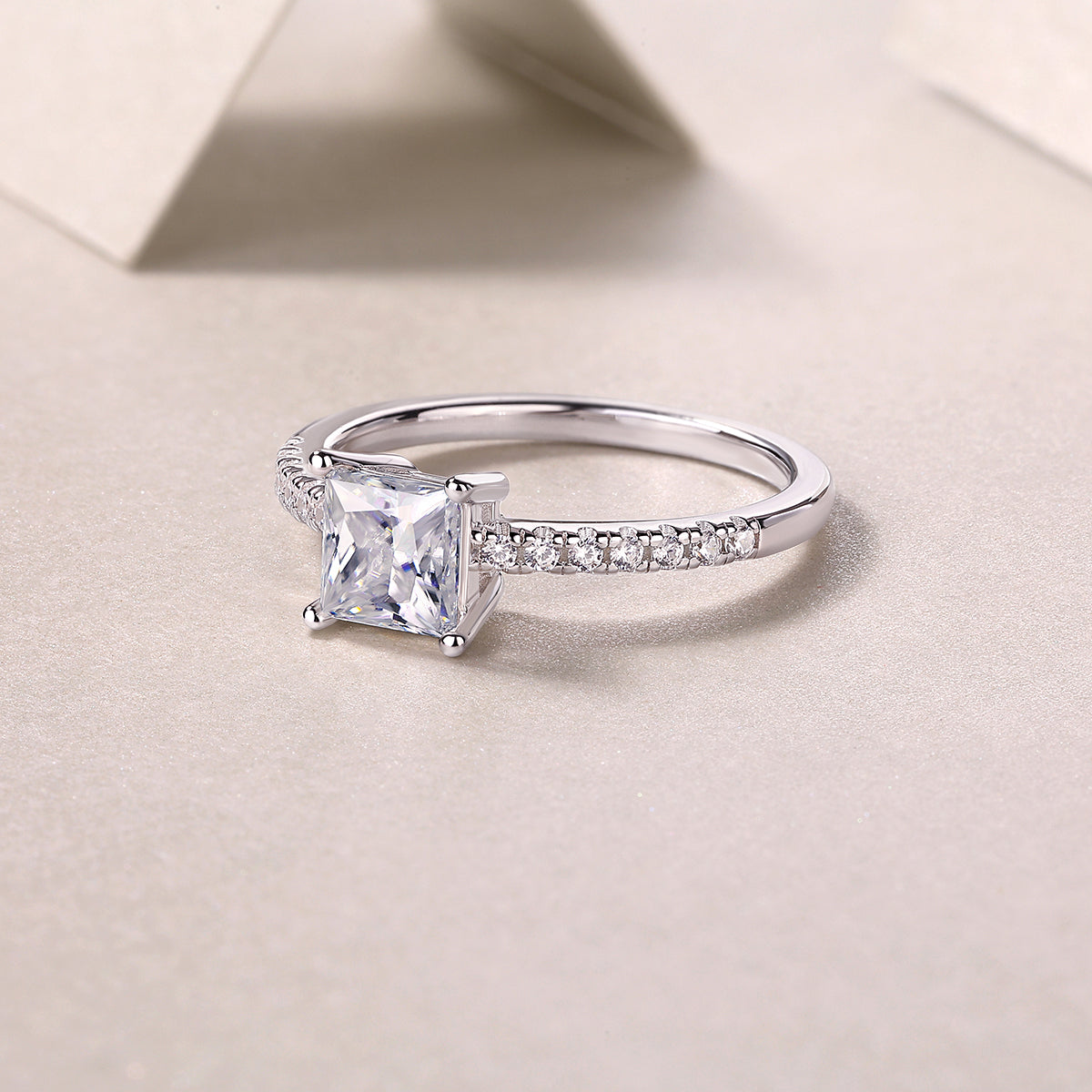 CARISSIE princess cut ring lifestyle shot on textured surface, capturing light reflection on silver metal and facets