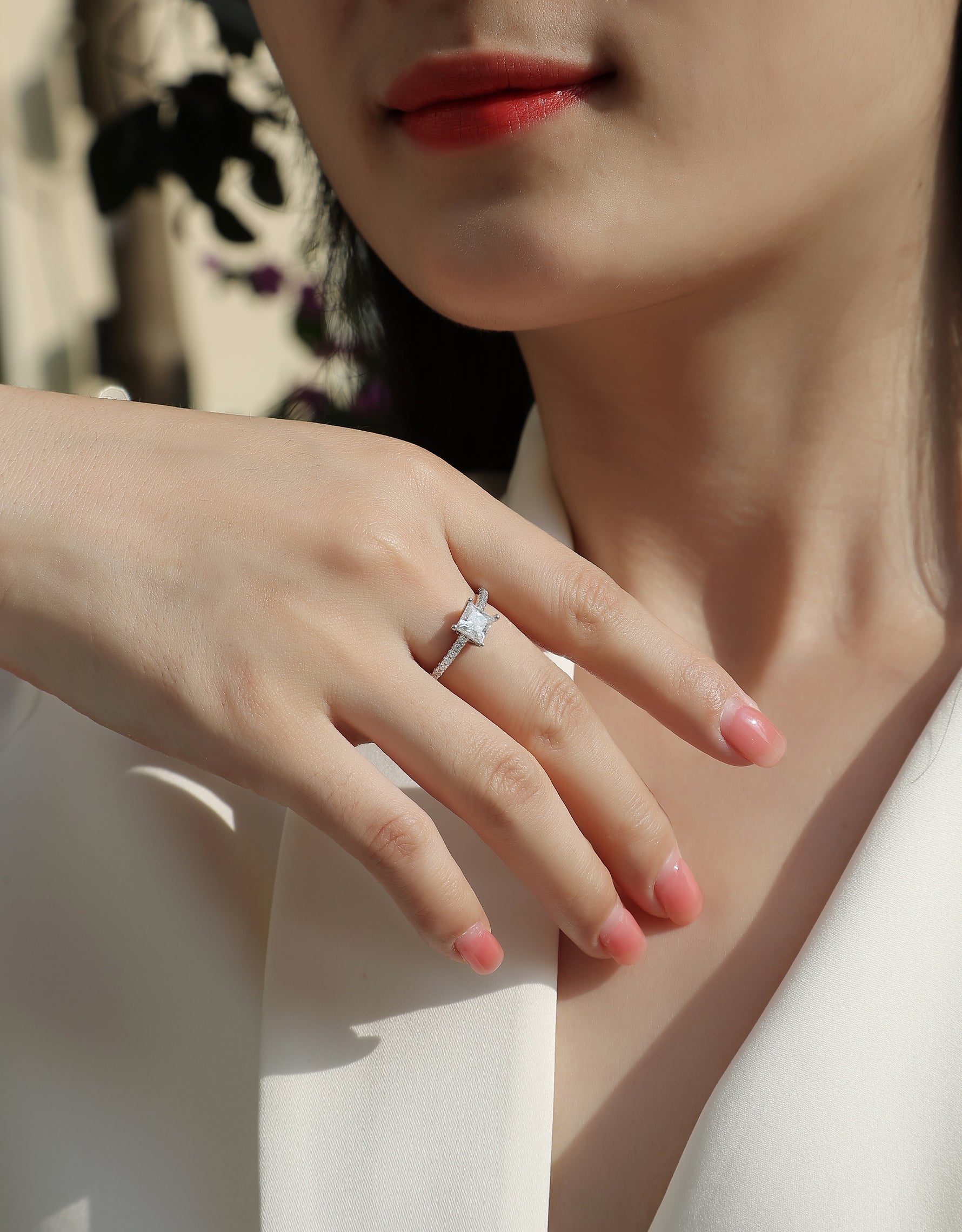 CARISSIE princess solitaire engagement ring on model hand, showing square stone and pavé band against white blazer