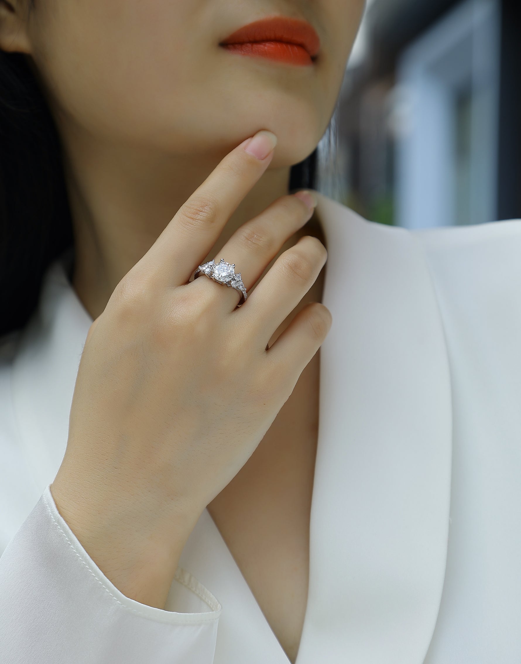 CARISSIE round moissanite solitaire ring on hand, showing side clusters and pavé band against white blazer