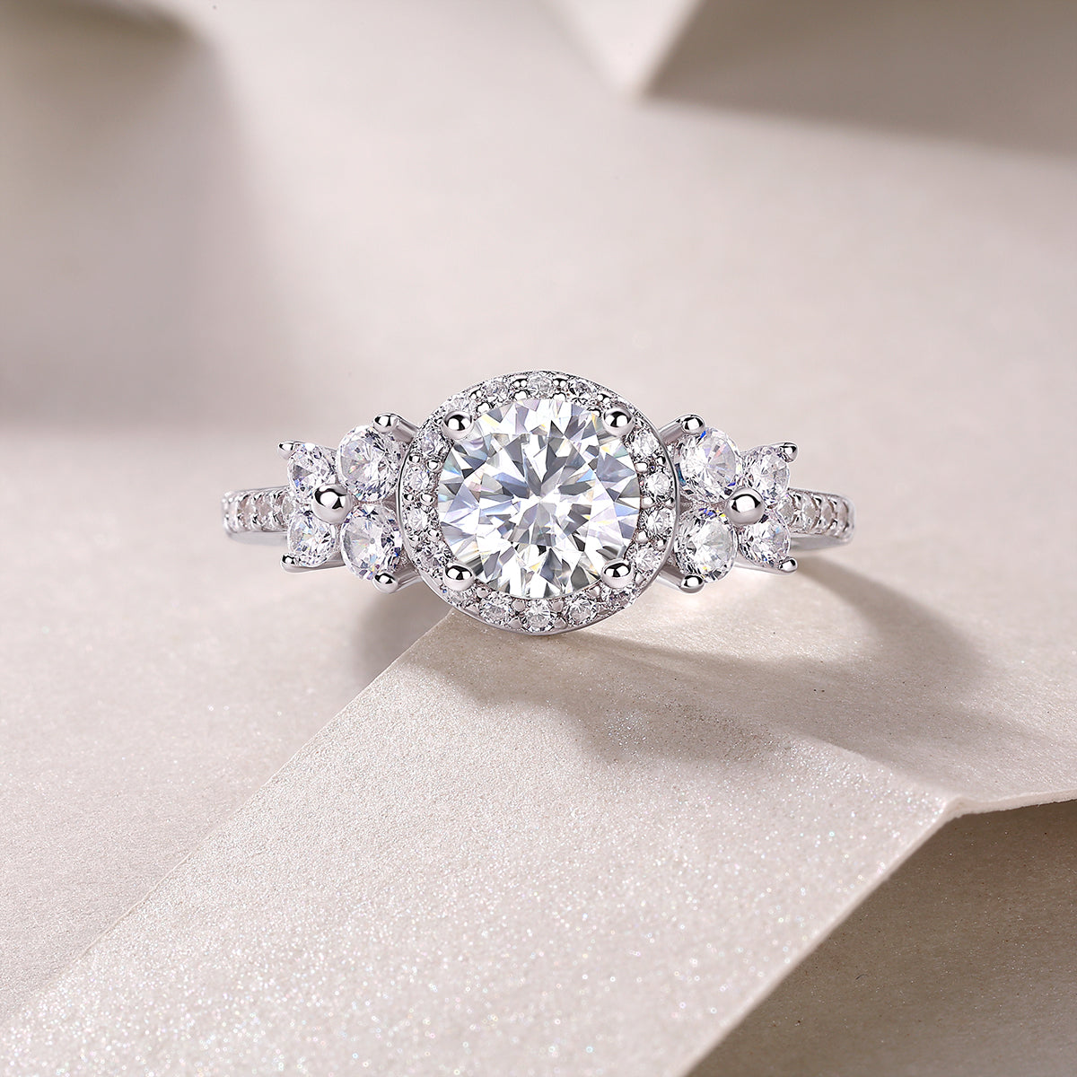 CARISSIE round moissanite halo engagement ring close-up on fabric, focusing on halo surround and petal-shaped stones