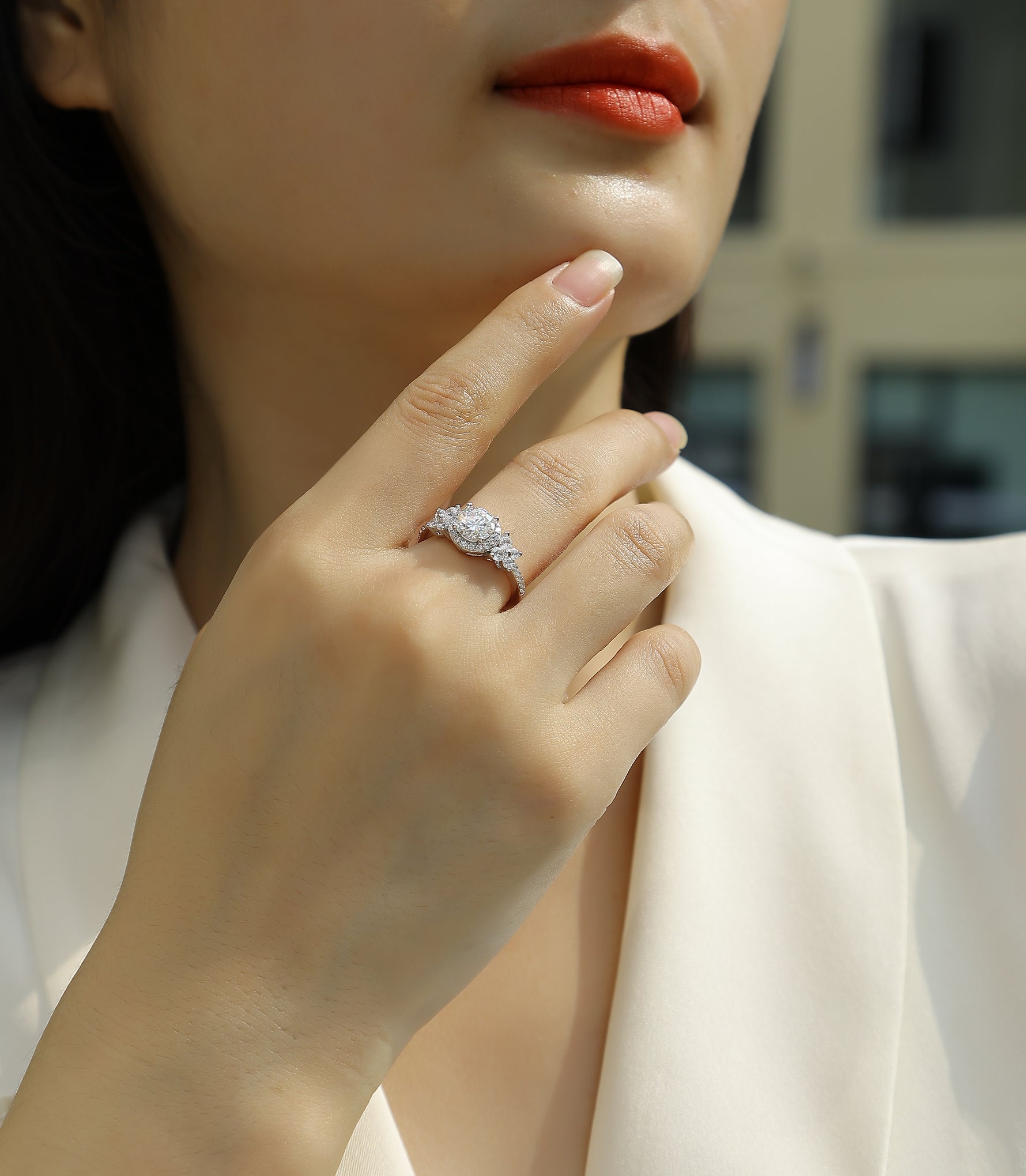 CARISSIE round moissanite halo engagement ring on model hand, highlighting floral side accents and white blazer styling