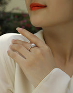 CARISSIE round moissanite halo ring on model hand, showing geometric octagonal setting and pavé band against white blazer