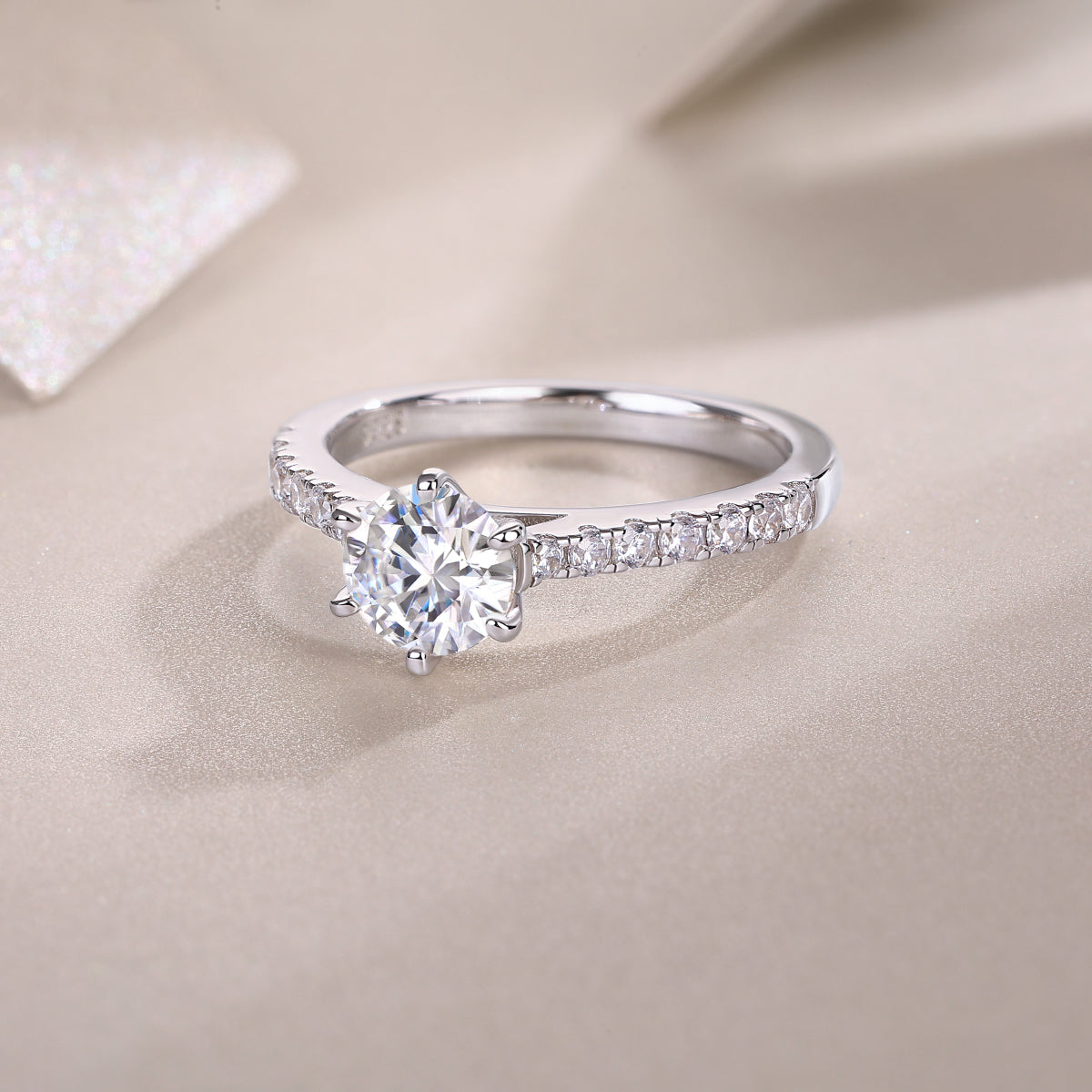 CARISSIE round moissanite solitaire ring, lifestyle shot on textured beige background with soft lighting