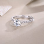 CARISSIE round moissanite solitaire ring, lifestyle shot on textured beige background with soft lighting