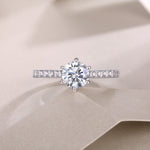 CARISSIE round moissanite solitaire ring, top-down perspective on fabric surface emphasizing sparkle and cut