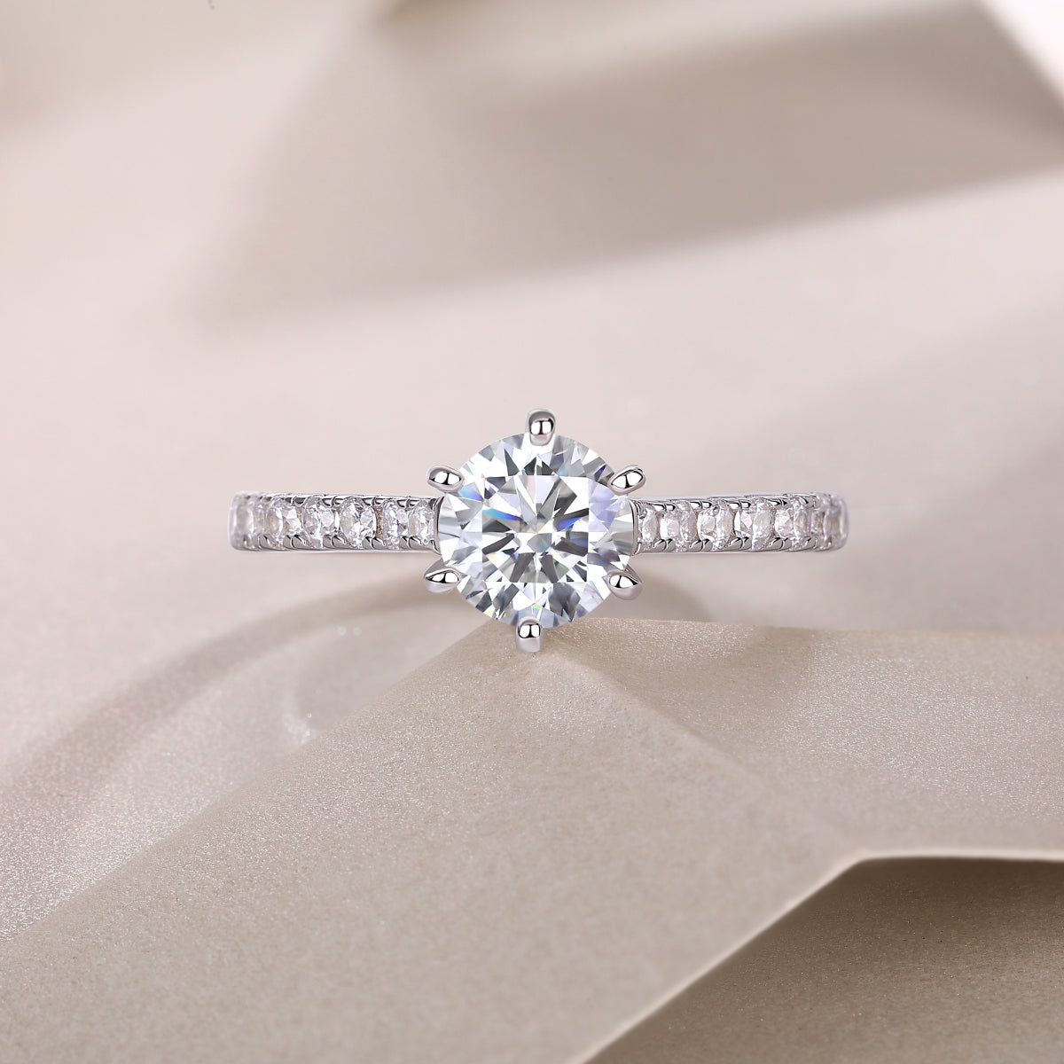 CARISSIE round moissanite solitaire ring, top-down perspective on fabric surface emphasizing sparkle and cut