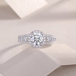 CARISSIE round moissanite solitaire ring, lifestyle shot on white textured surface emphasizing sparkle and intricate details