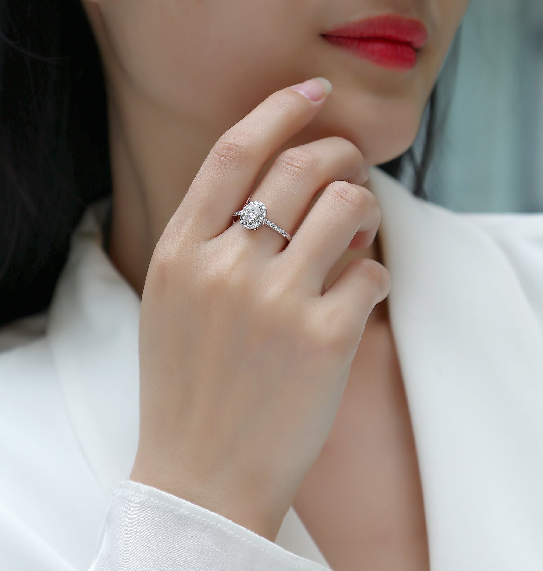CARISSIE oval moissanite halo engagement ring worn on finger, close-up view of setting against skin