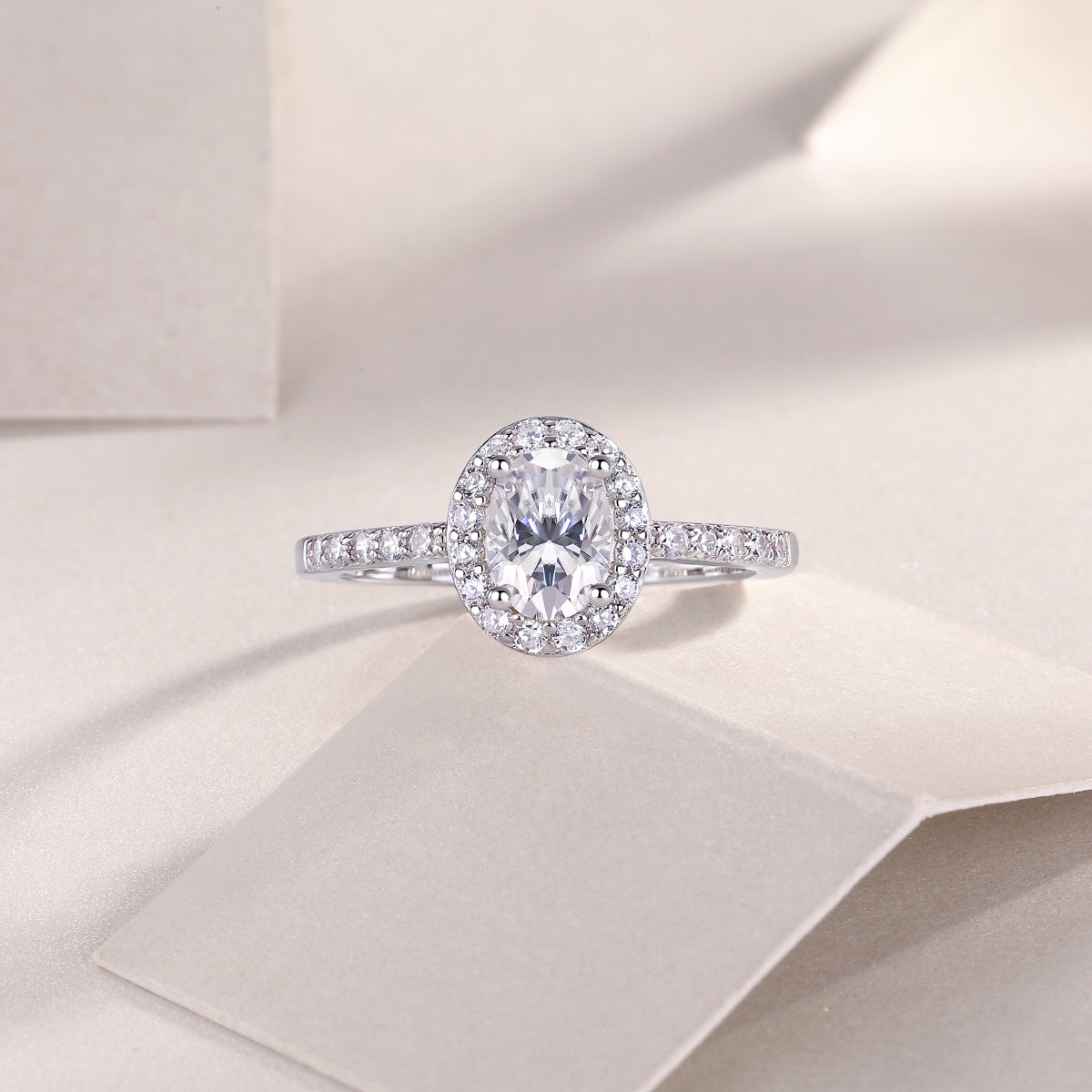 CARISSIE oval moissanite halo engagement ring resting on textured beige surface with soft lighting shadows