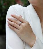 CARISSIE oval moissanite halo ring on model hand resting on shoulder, showing silver-tone setting and pavé band