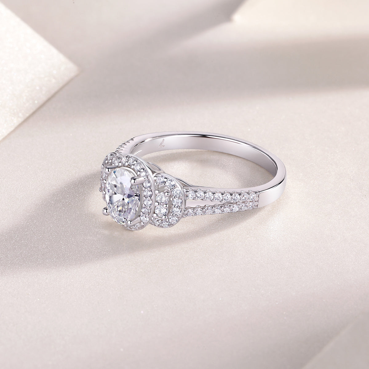 CARISSIE oval moissanite halo ring resting on textured surface, showcasing polished inner band and side stones