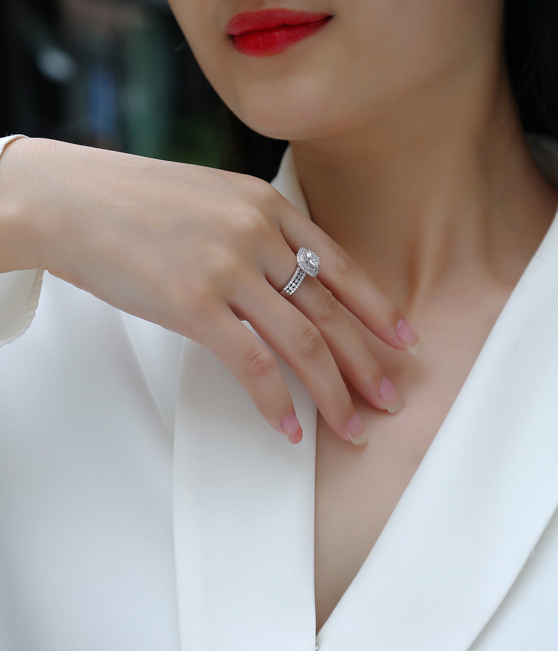 CARISSIE round moissanite halo engagement ring, lifestyle shot on hand resting on white blazer lapel