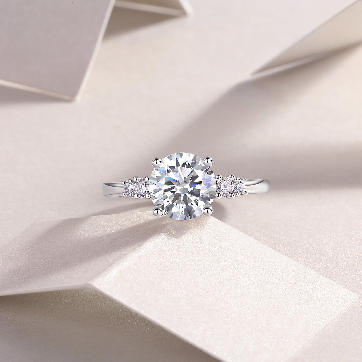 CARISSIE round moissanite solitaire ring, lifestyle shot on textured white surface showcasing the sparkle of the center diamond