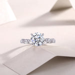 CARISSIE round moissanite solitaire ring, lifestyle shot on textured paper with soft lighting emphasizing stone brilliance