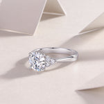 CARISSIE round moissanite solitaire ring, oblique angle emphasizing curved band design and sparkle of clustered side stones