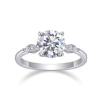 CARISSIE round moissanite solitaire ring, front view displaying large center stone in four-prong setting with side clusters