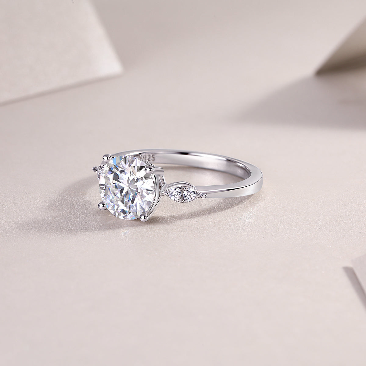 CARISSIE round moissanite solitaire ring, lifestyle shot on textured surface showing interior hallmark and smooth metal finish