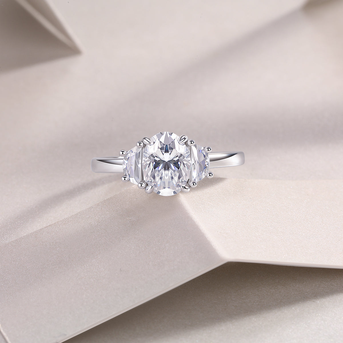 CARISSIE oval moissanite solitaire ring, lifestyle shot on textured beige paper emphasizing the sparkle of the gemstones