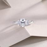 CARISSIE oval moissanite solitaire ring, lifestyle shot on textured beige paper emphasizing the sparkle of the gemstones