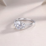 CARISSIE oval moissanite solitaire ring, soft-focus lifestyle image showcasing the ring's curve and metal finish on fabric