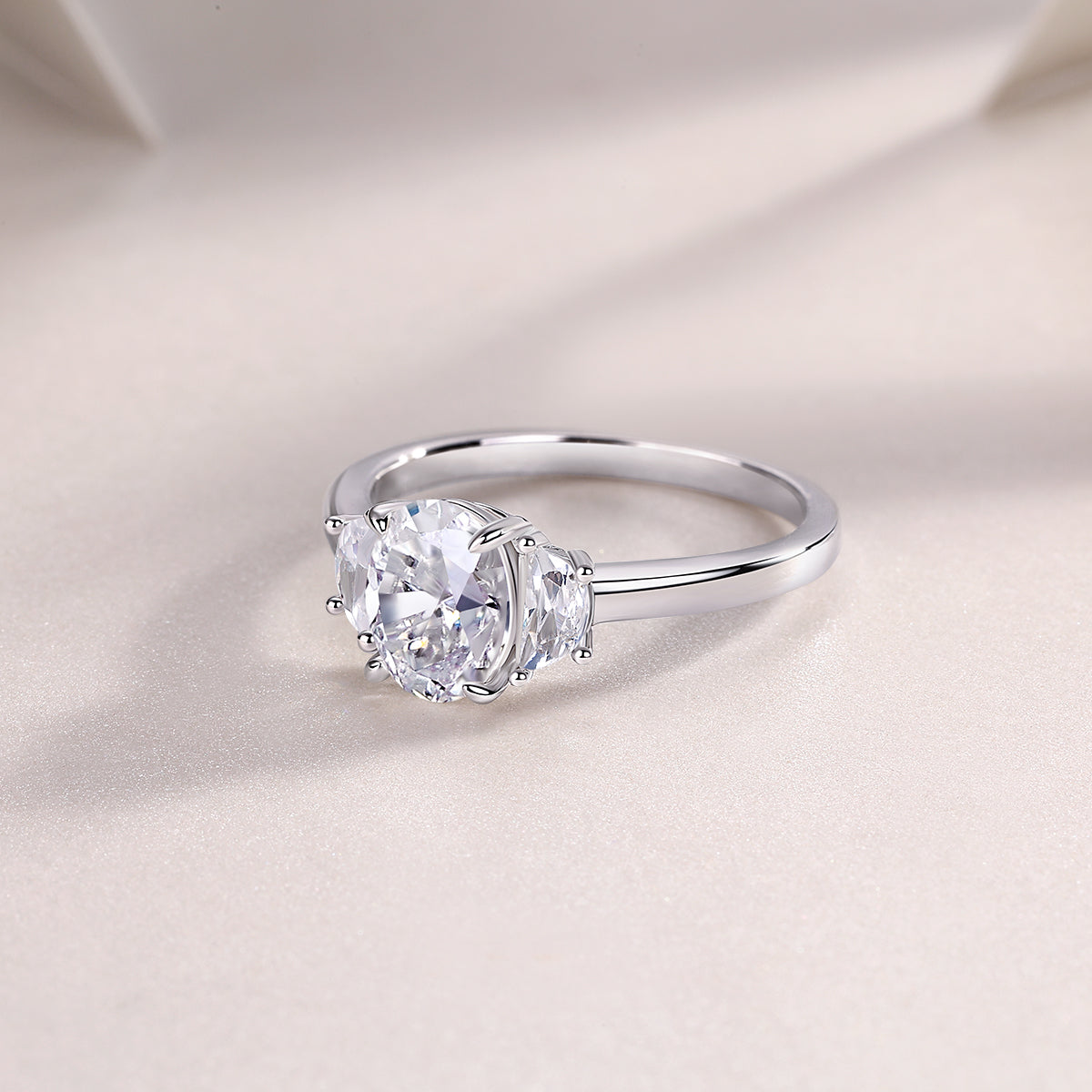 CARISSIE oval moissanite solitaire ring, soft-focus lifestyle image showcasing the ring's curve and metal finish on fabric