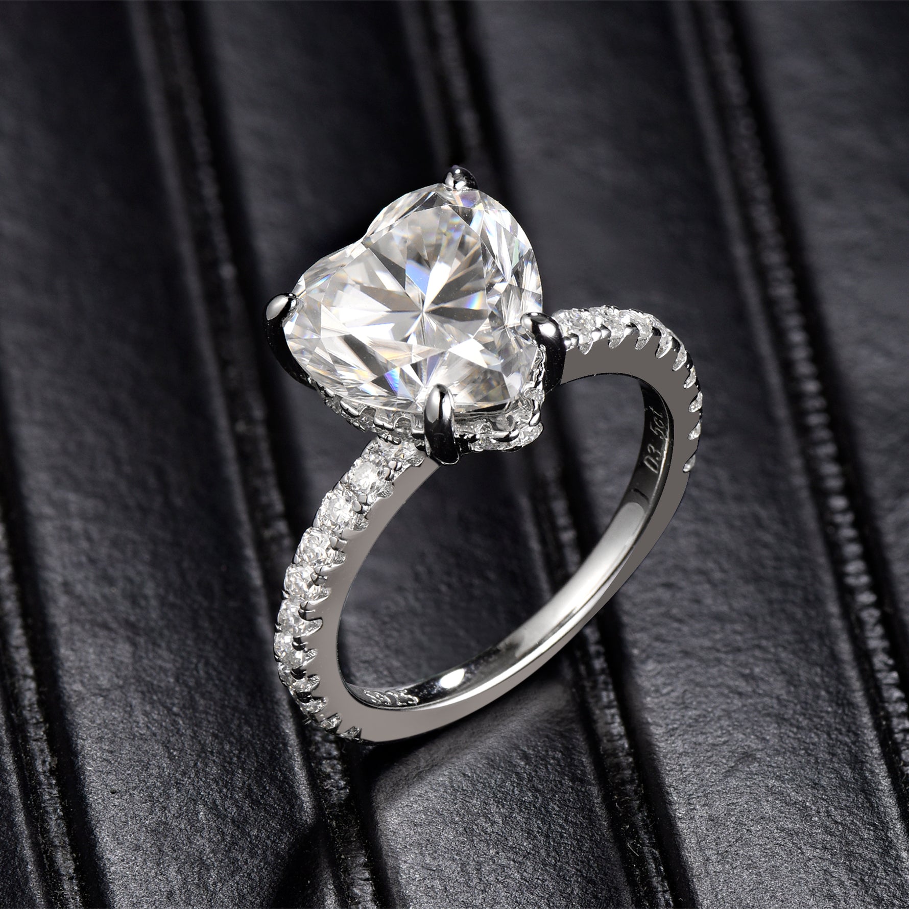 CARISSIE heart solitaire engagement ring, angled view on black leather showing pavé band and four-prong setting