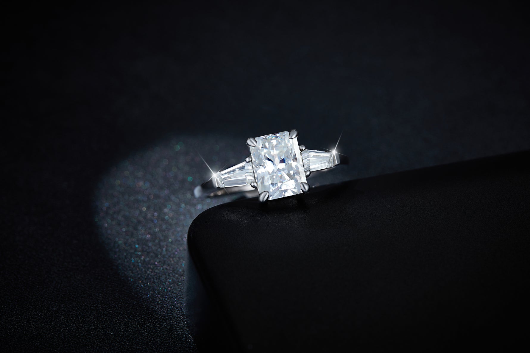 CARISSIE moissanite three-stone ring, elevated front angle displaying the brilliant rectangular center gemstone and prong setting details