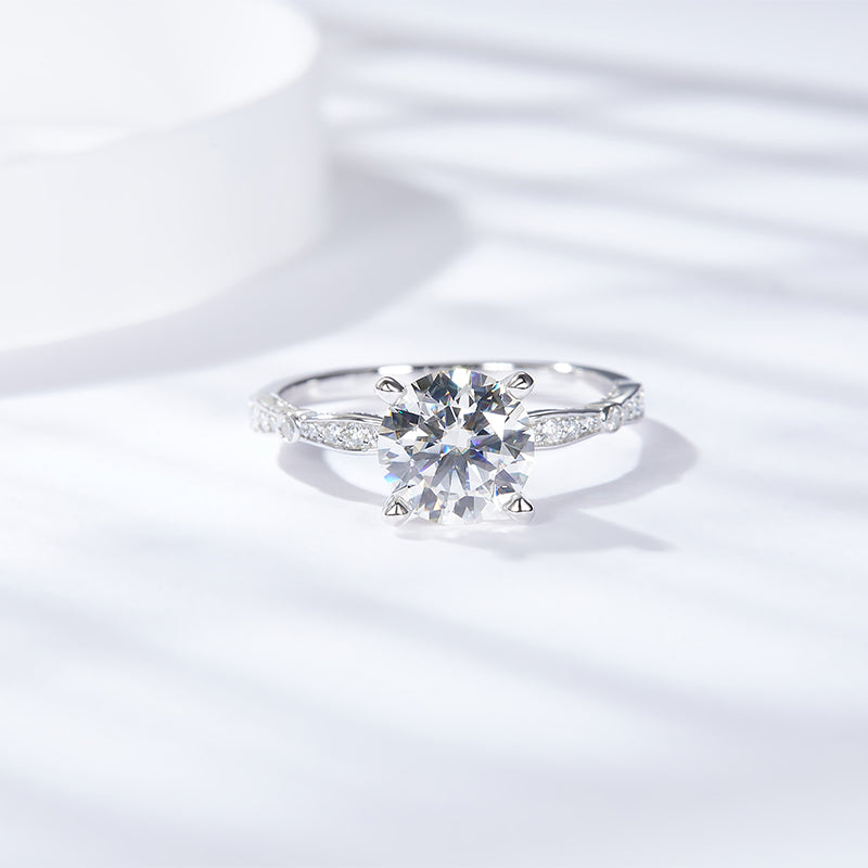 CARISSIE round moissanite solitaire ring, top-down perspective revealing symmetrical prongs and diamond accents in bright light