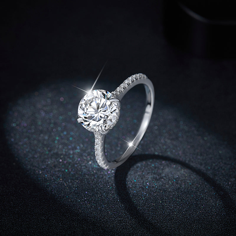 CARISSIE round moissanite solitaire ring, lifestyle shot against dark glitter background showcasing intense sparkle and light reflection