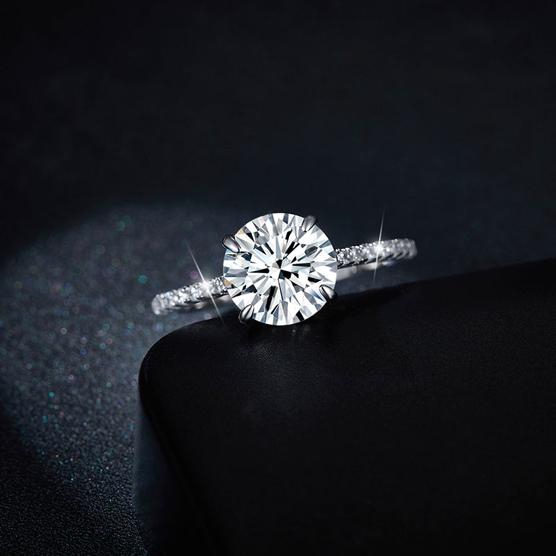 CARISSIE round moissanite solitaire ring, dramatic close-up resting on black surface emphasizing fire dispersion in the large center gem