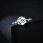CARISSIE round moissanite solitaire ring, dramatic close-up resting on black surface emphasizing fire dispersion in the large center gem