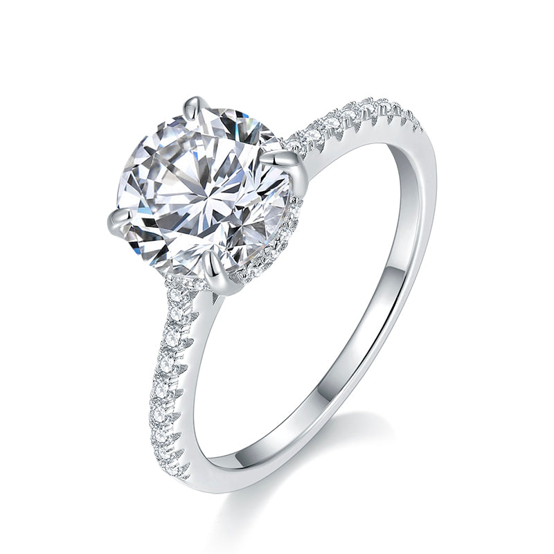 CARISSIE round moissanite solitaire ring, angled view highlighting four-prong setting and pavé diamond band on polished silver-tone metal