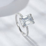 CARISSIE emerald cut solitaire engagement ring, angled view highlighting step-cut facets and pavé band