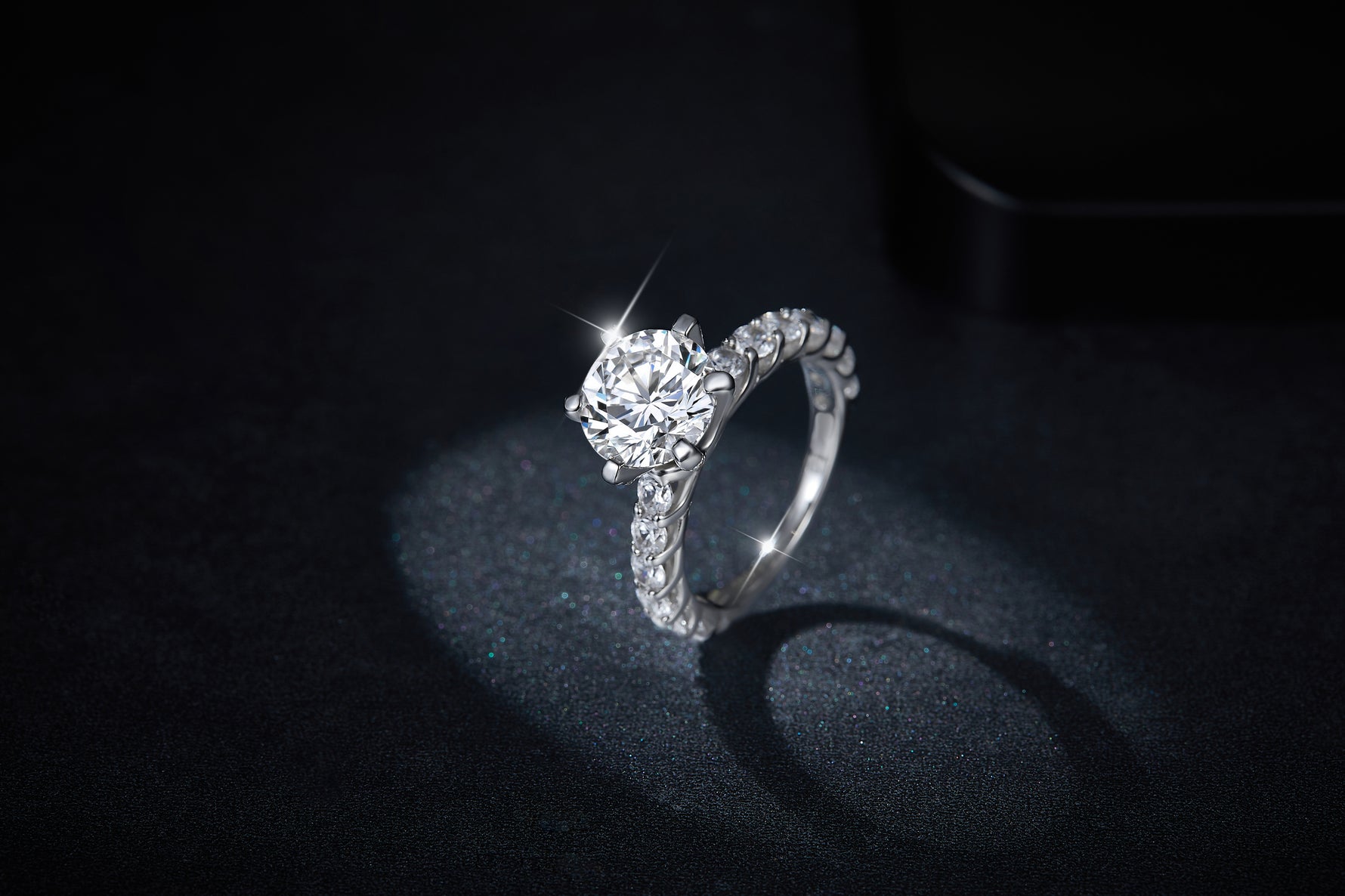 CARISSIE round moissanite solitaire ring, angled lifestyle shot on dark glittery background emphasizing the sparkle of the main gemstone