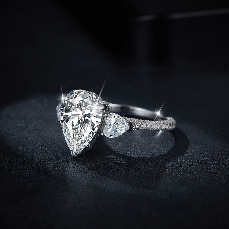 CARISSIE pear moissanite solitaire ring, dramatic dark background shot emphasizing the brilliance of the stones