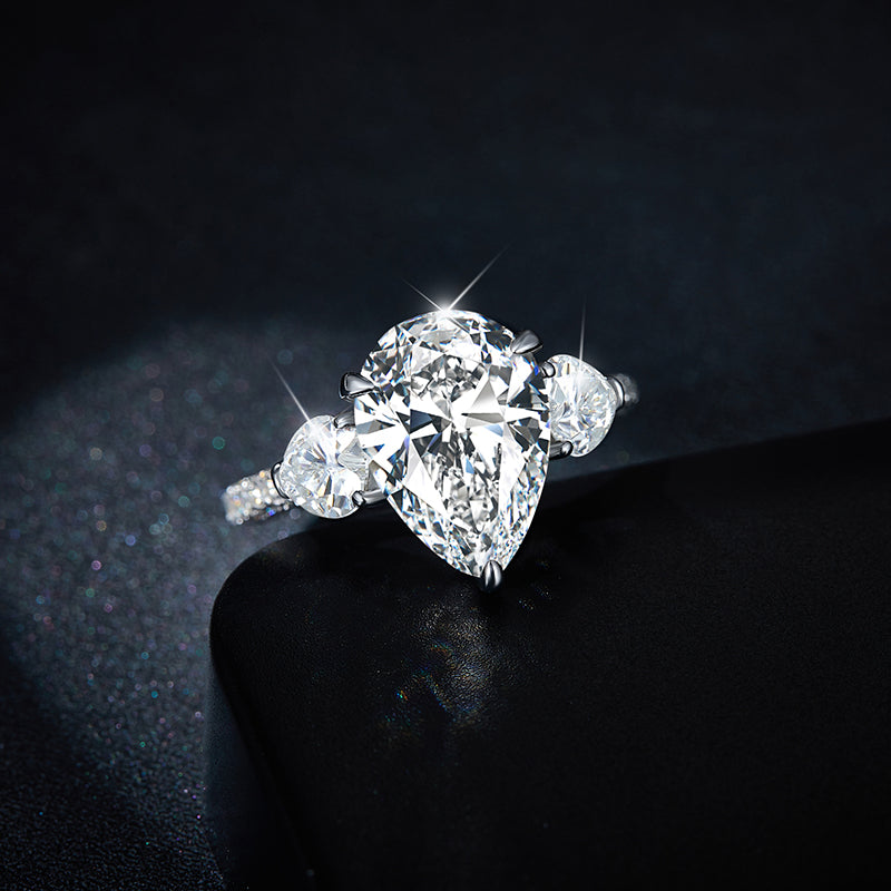 CARISSIE pear moissanite solitaire ring, resting on black display surface with light reflecting off the facets