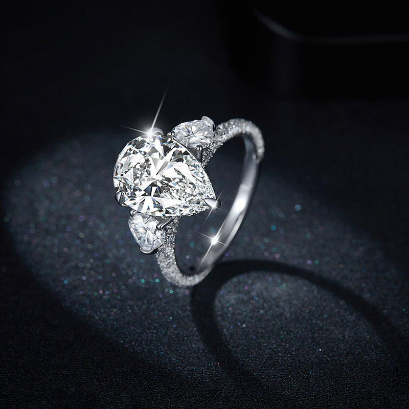 CARISSIE pear moissanite solitaire ring, high-angle close-up showcasing the sparkle against a glittering backdrop