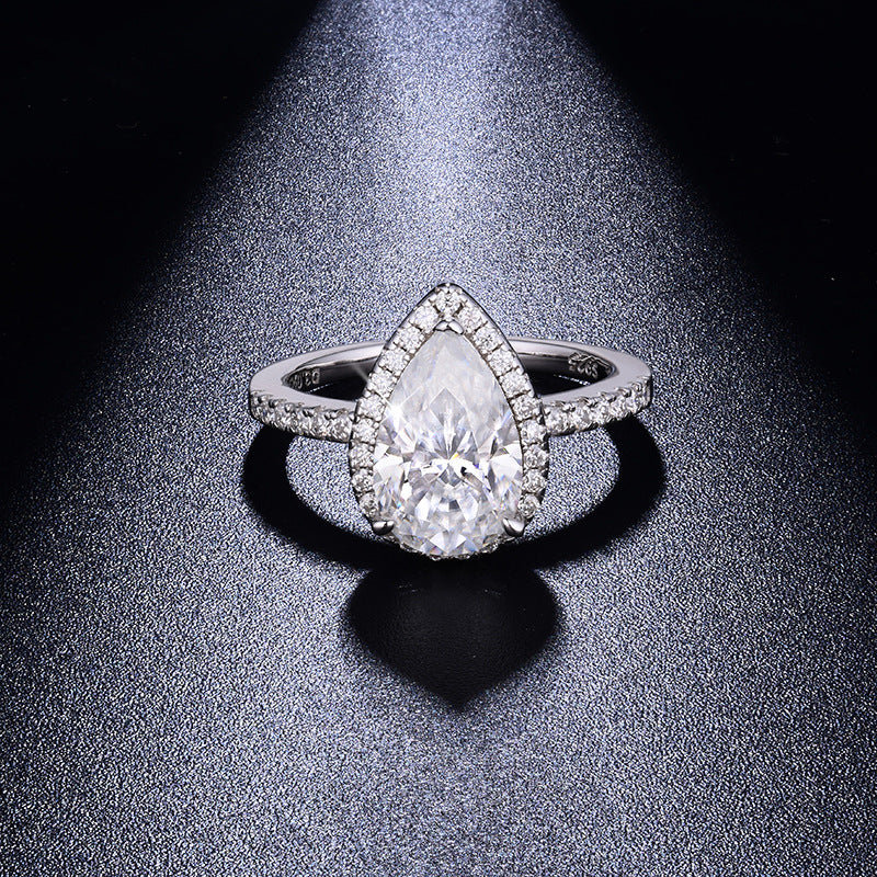 CARISSIE pear moissanite halo ring, front view on dark textured background highlighting the brilliant center stone and diamond-encrusted split shank