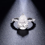 CARISSIE pear moissanite solitaire ring, dramatic spotlight view emphasizing the brilliance of the faceted center gem