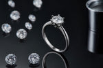 CARISSIE round moissanite solitaire ring, standing upright next to loose gems, showcasing the high-polish finish of the metal