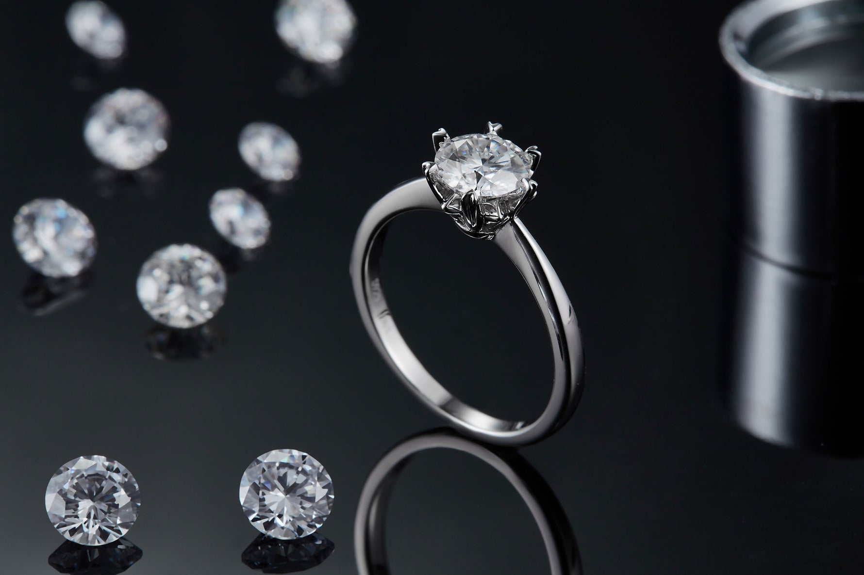 CARISSIE round moissanite solitaire ring, standing upright next to loose gems, showcasing the high-polish finish of the metal