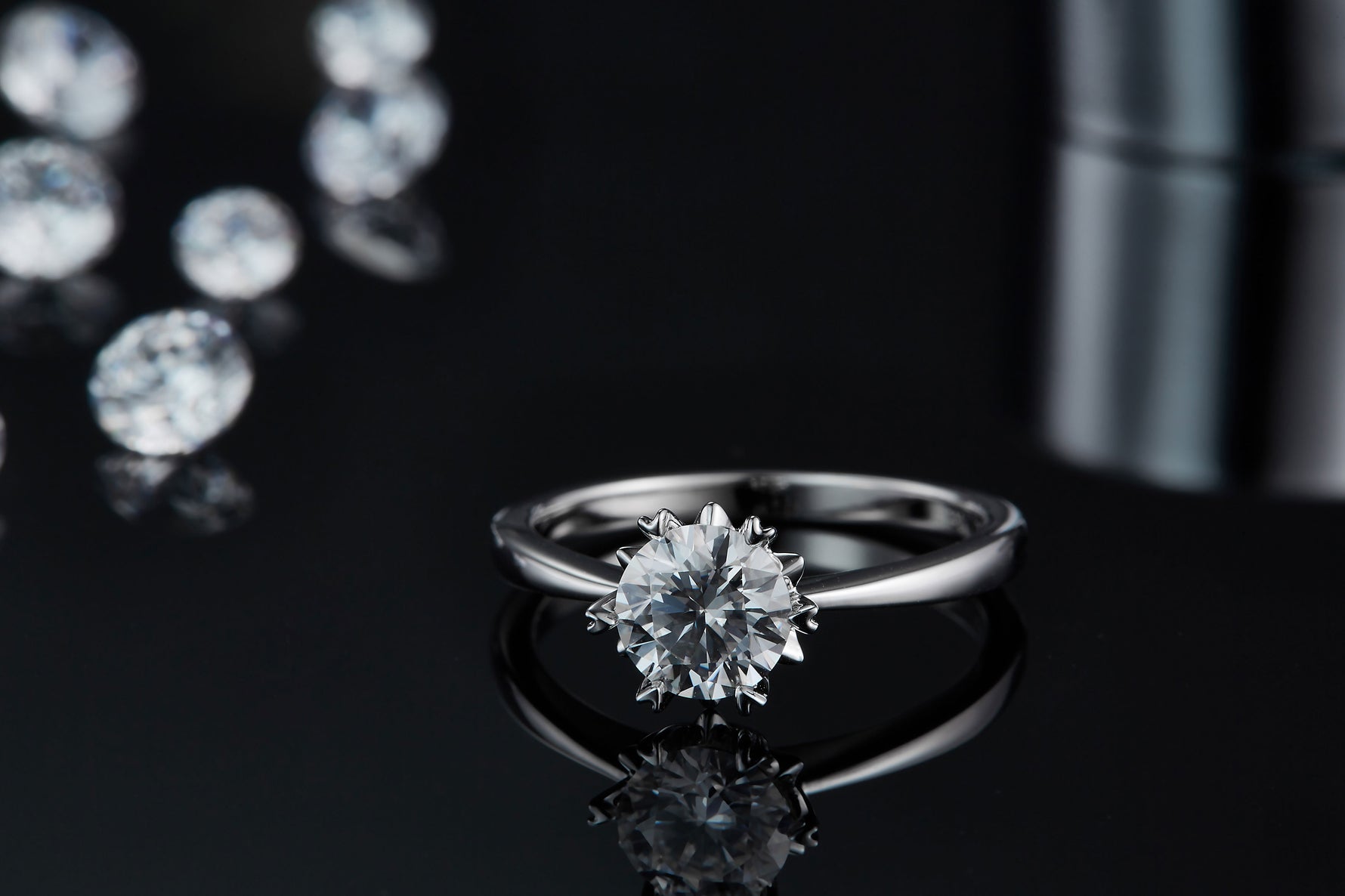 CARISSIE round moissanite solitaire ring, lifestyle shot on a dark reflective surface with scattered loose stones in background